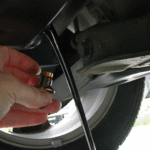 Sump plug being removed from a sump and oil flowing out.