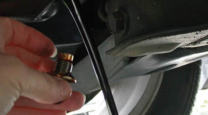 Sump plug being removed from a sump and oil flowing out.